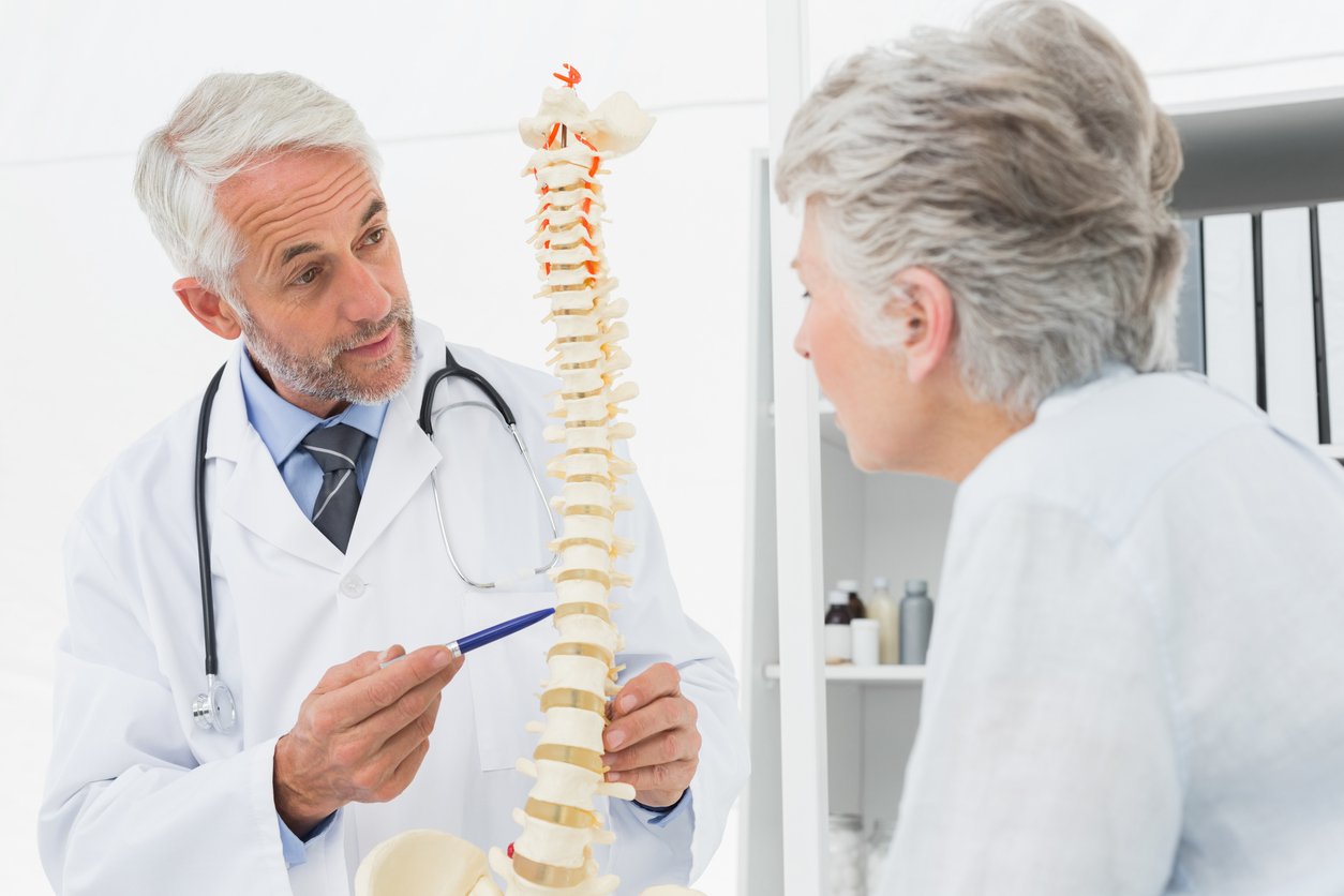 Male doctor explaining the spine to senior patient in medical office