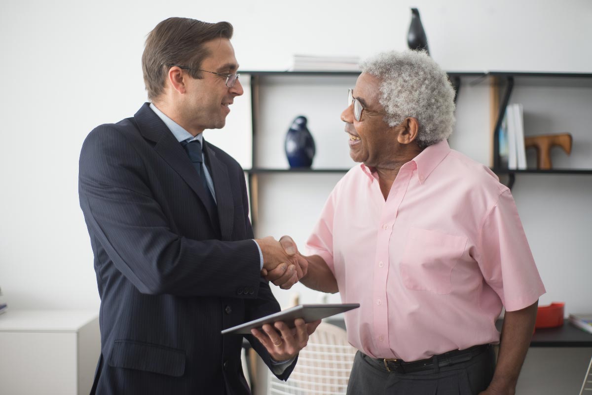 Two men shaking hands in an office. One dressed in a suit and one is dressed casually.
